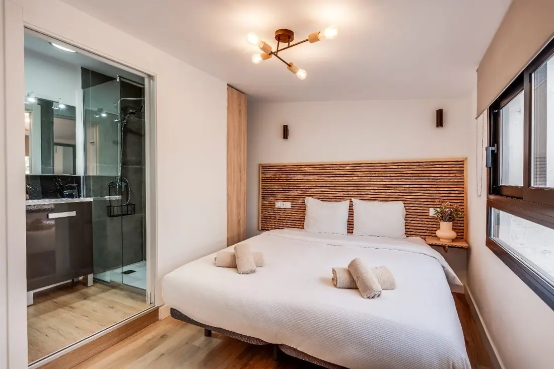The bedroom: a wide bed against an oak slat headboard, lit by a brass ceiling light