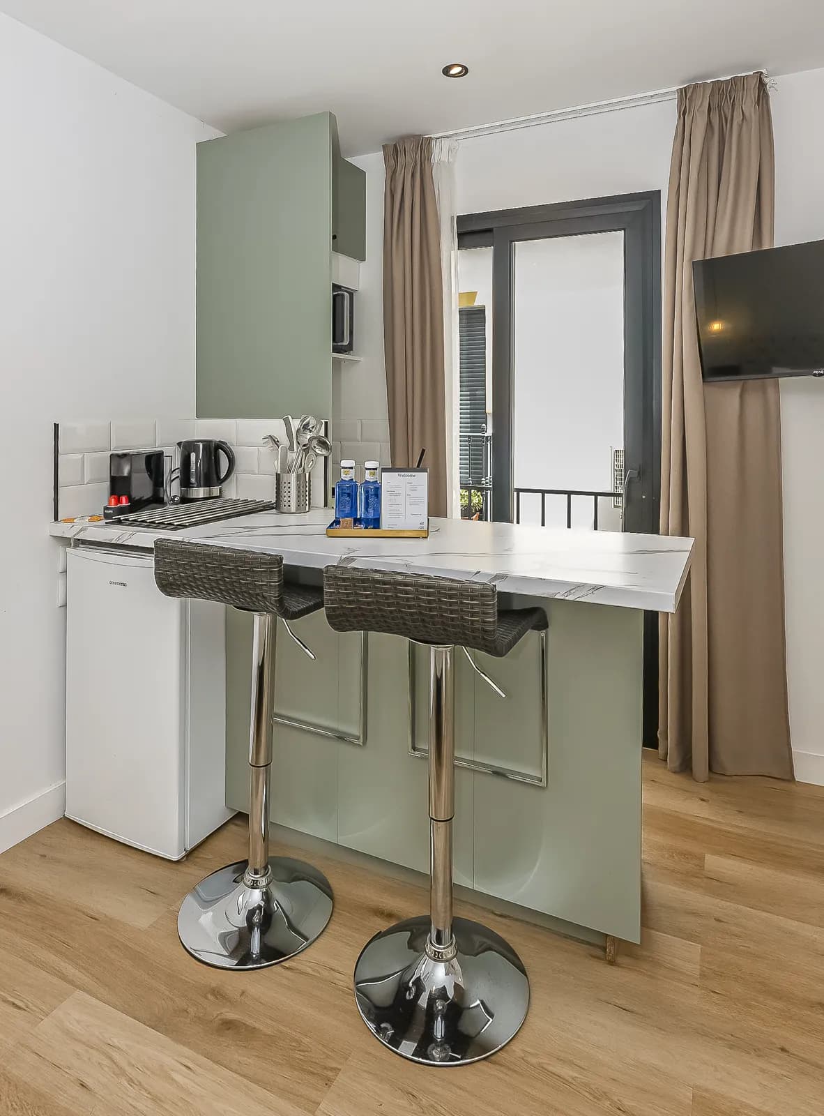 The kitchenette of a Signature Suite in sage green, with a microwave and a marble bar with two stools