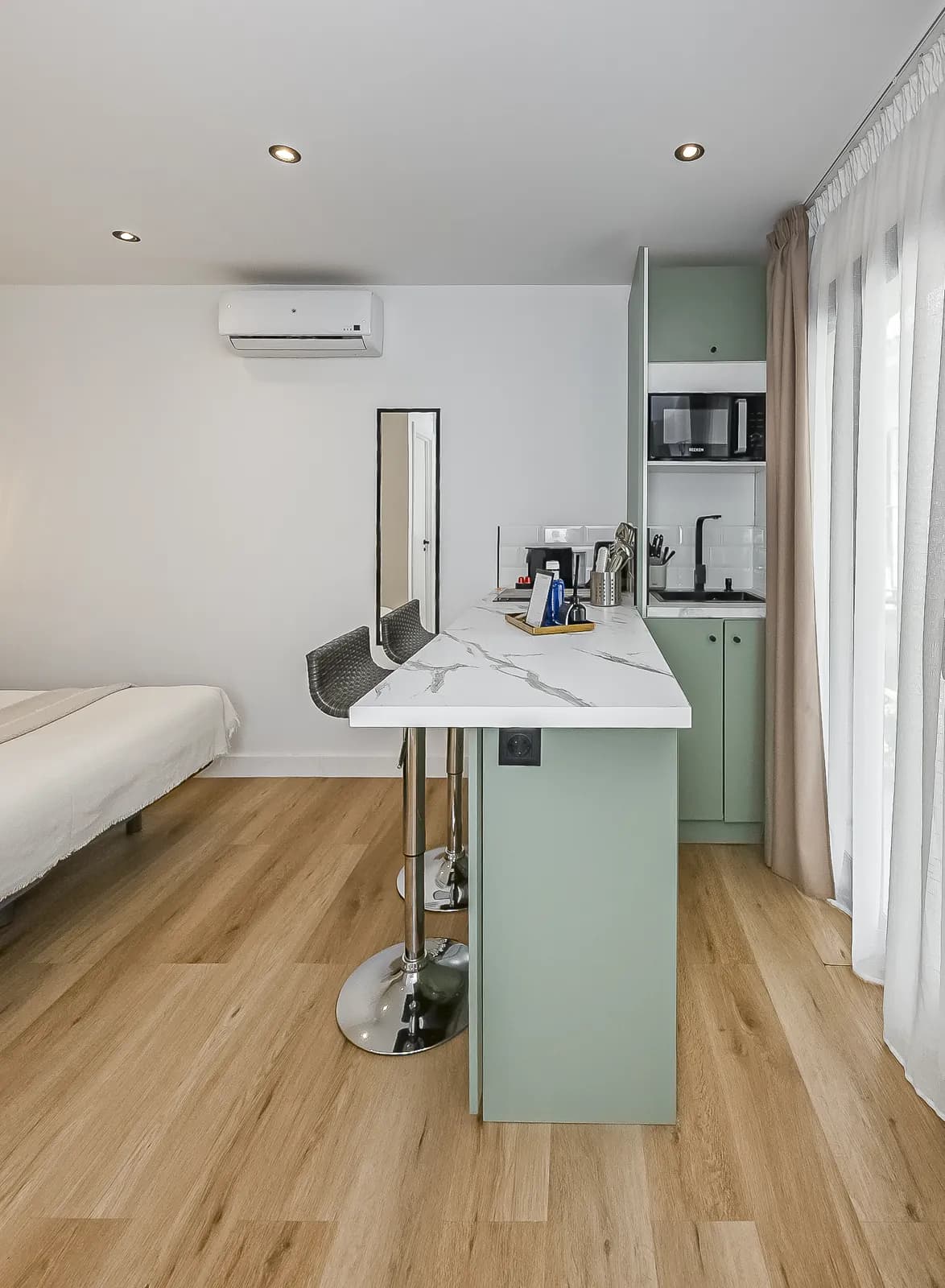 Room 1: the sage green kitchenette and the marble breakfast bar, with the bed beyond and the curtained window to the right