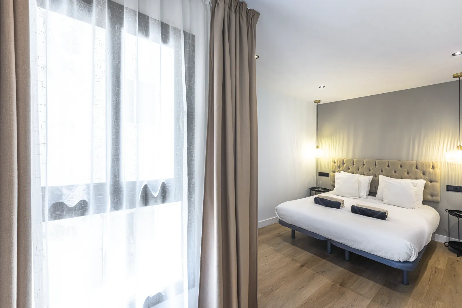 Room 2: the bed beside a tall window in linen curtains, with reading lights on the headboard wall