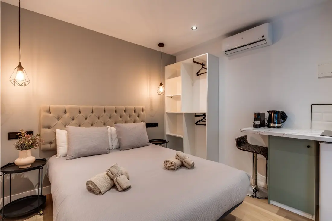 The Micro Suite: a bed with a tufted headboard and pendant lights, with open shelving and a marble counter along the right wall